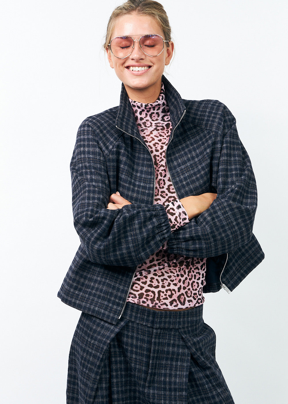 Person wearing a checked wool outfit with a jacket and pleated pants with a leopard print pink top on a white background