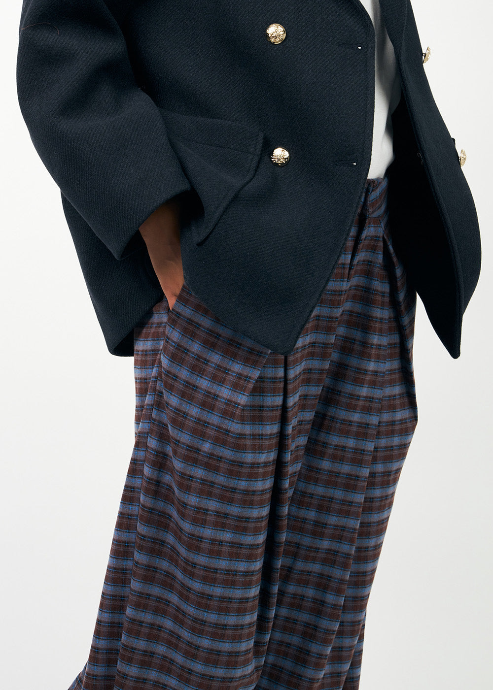 Person wearing a navy coat with gold buttons and plaid pants on a white background