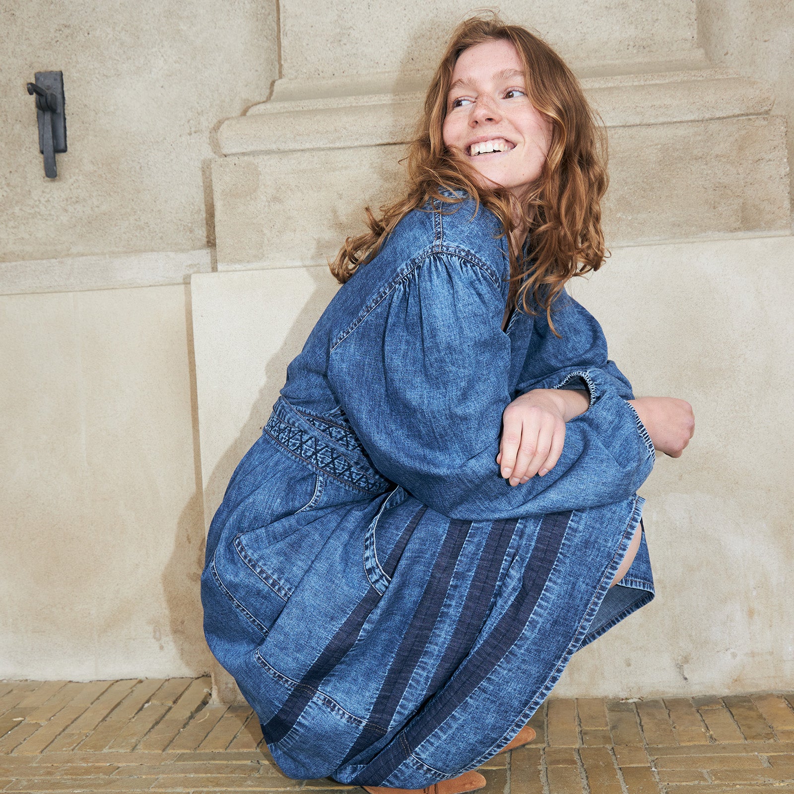 Woman wearing a blue denim dress with embroidered details and wide sleeves. A relaxed and feminine denim look for everyday wear.